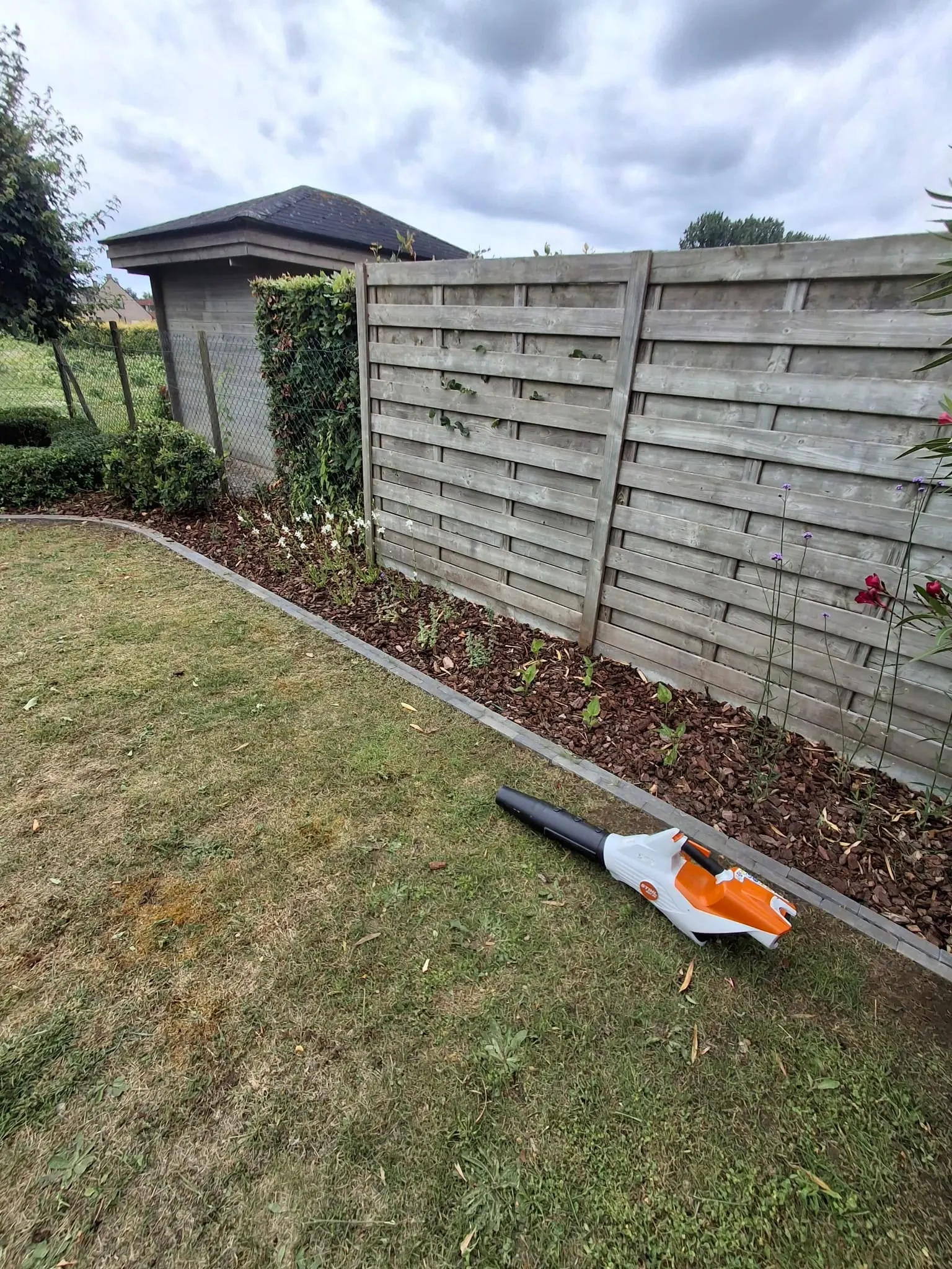Nieuw aangeplante border met houtschors langs een houten schutting en een gebogen boordsteen