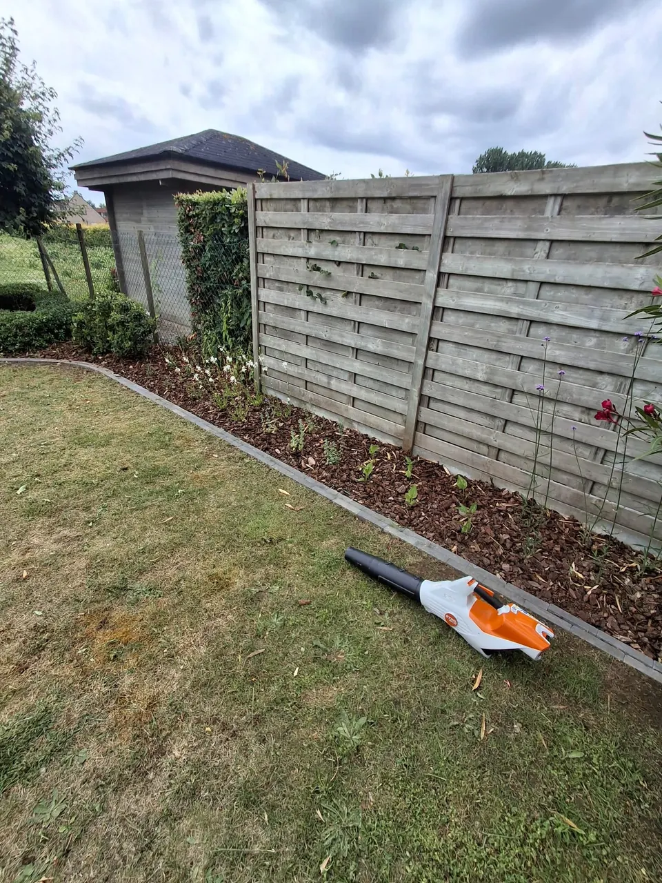 Nieuw aangeplante border met houtschors langs een houten schutting en een gebogen boordsteen