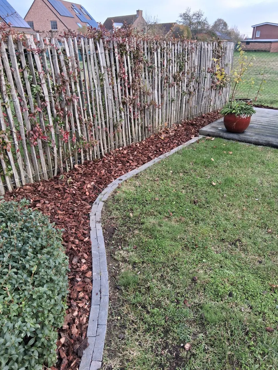 Gebogen border met houtschors langs een kastanjehouten hek