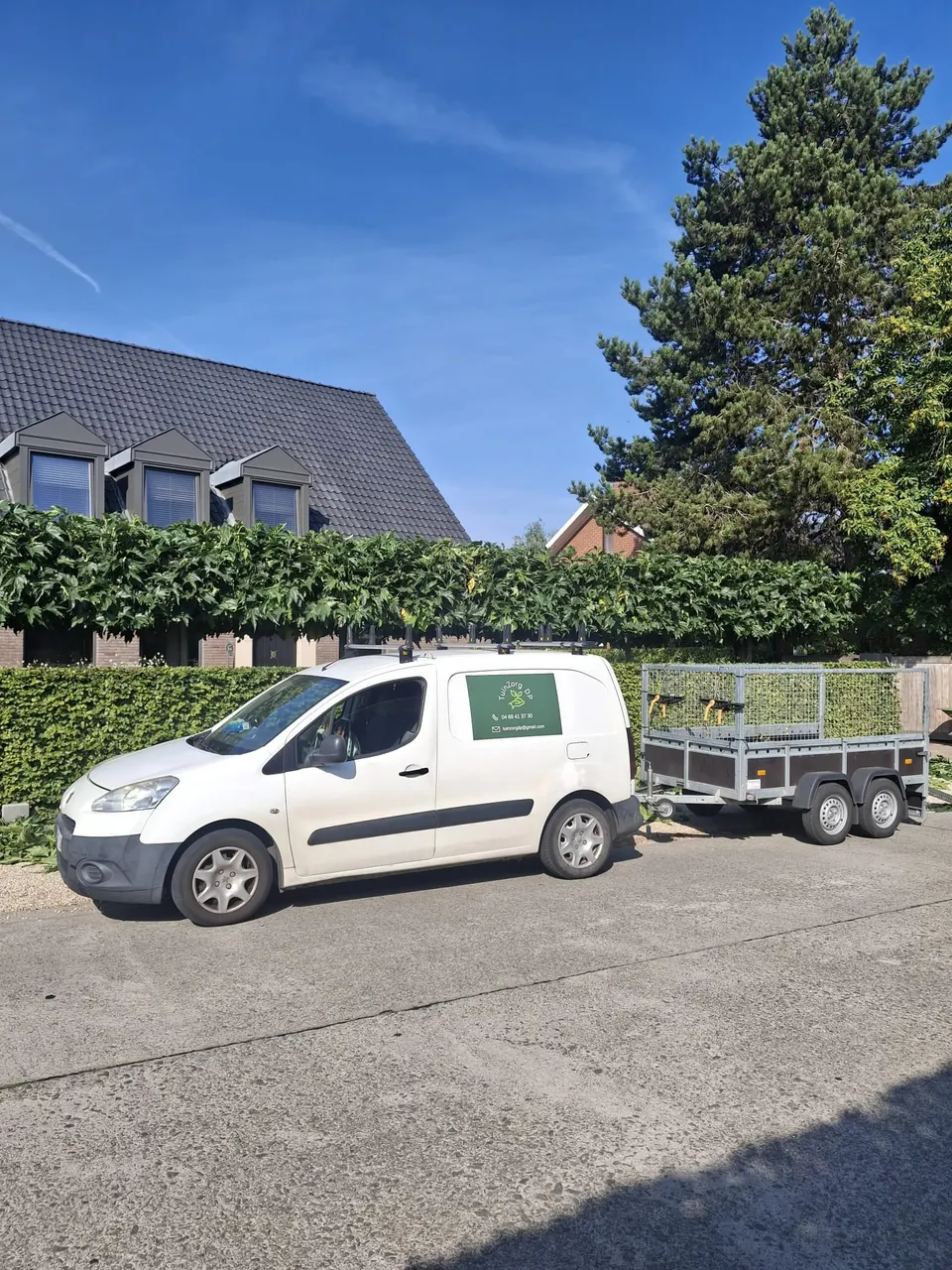 Bestelwagen met aanhangwagen op een oprit voor een gesnoeide haag