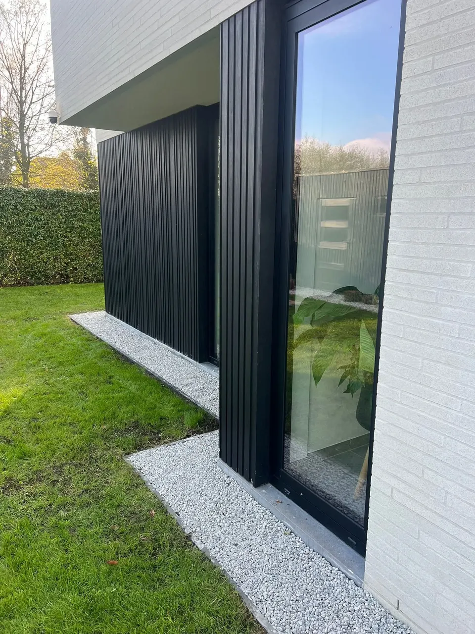 Strook wit grind met stalen boordrand langs een moderne gevel en het gazon