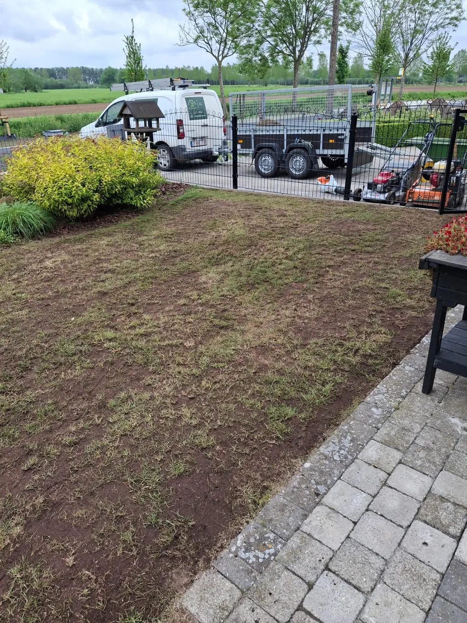 Geverticuteerde voortuin met aanhangwagen en bestelwagen op de achtergrond