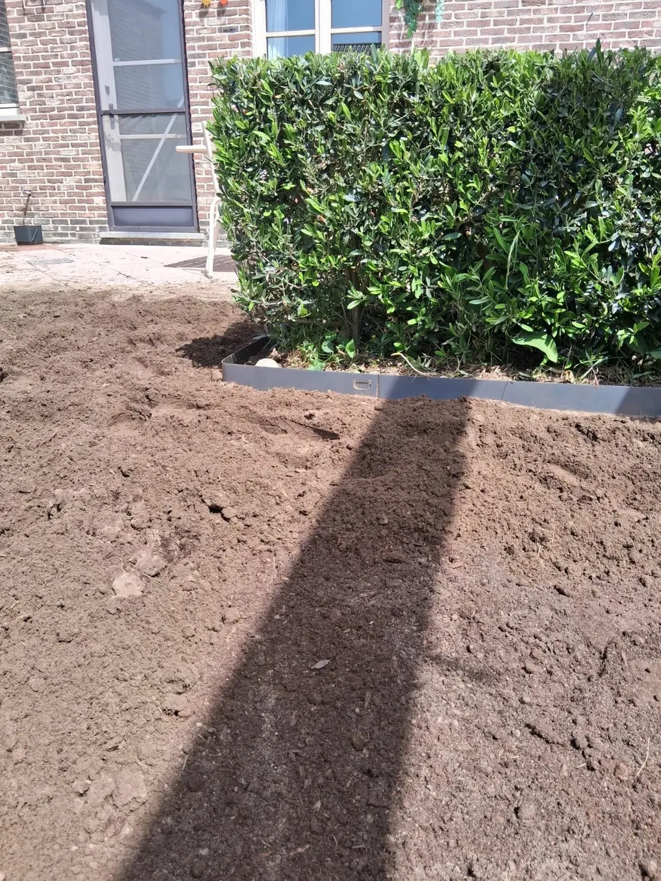 Stalen tuinafboording rond een haag, met vers aangevulde tuingrond