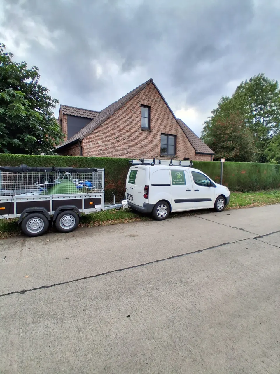 Witte bestelwagen van TuinZorg DP met aanhangwagen voor een woning