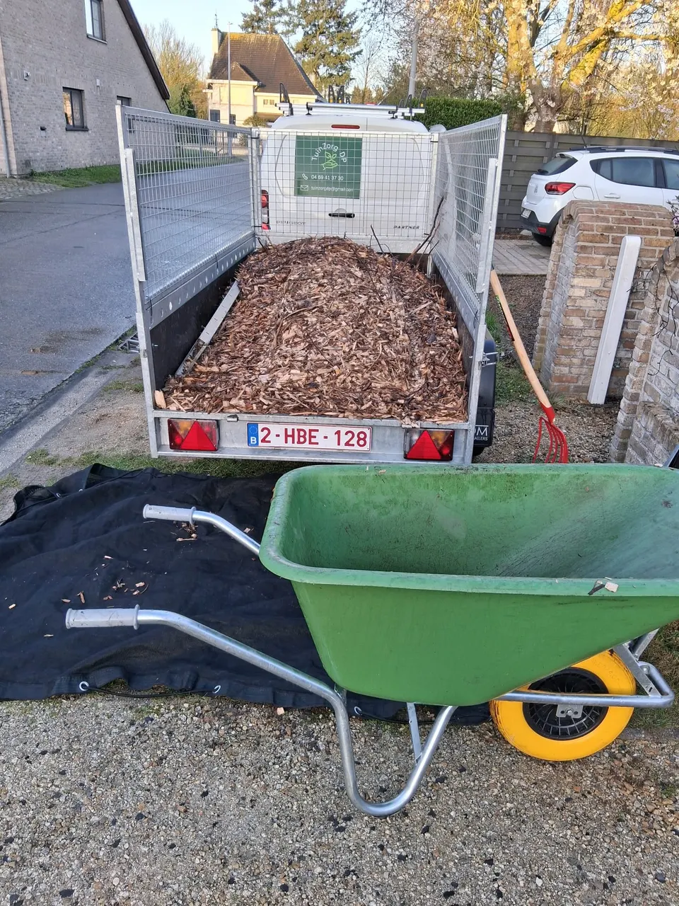 Aanhangwagen vol houtschors met een groene kruiwagen ervoor