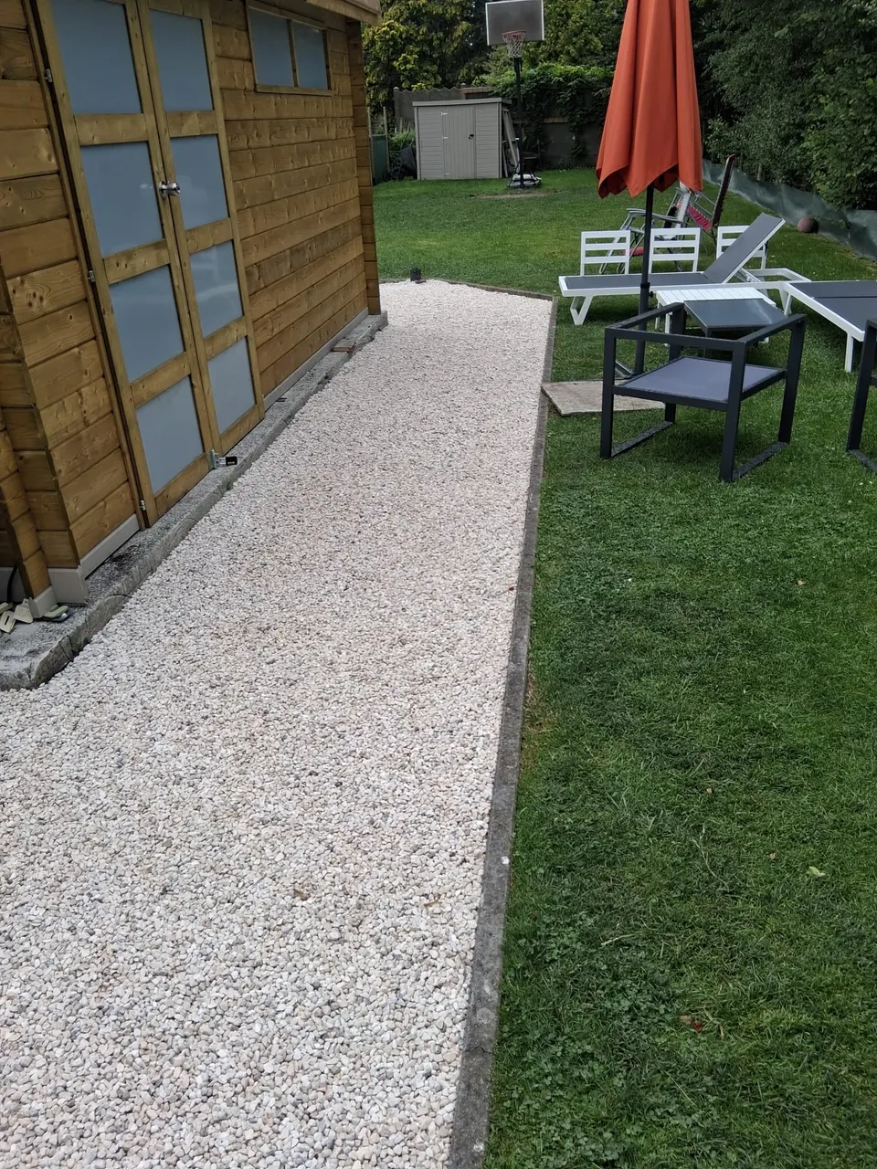 Wit grindpad langs een houten tuinhuis en het gazon