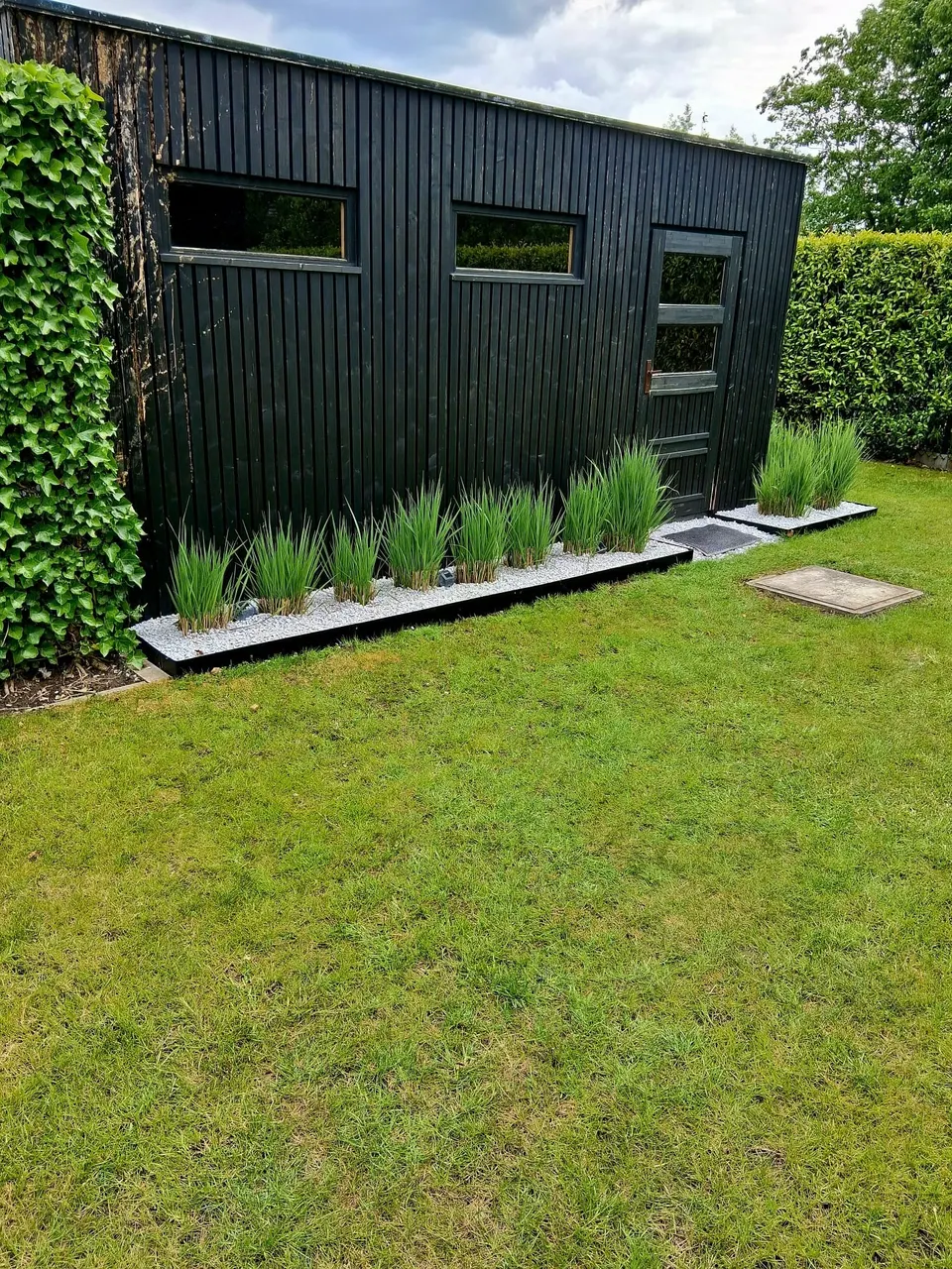 Rechte afboording met siergrassen voor een zwart tuinhuis